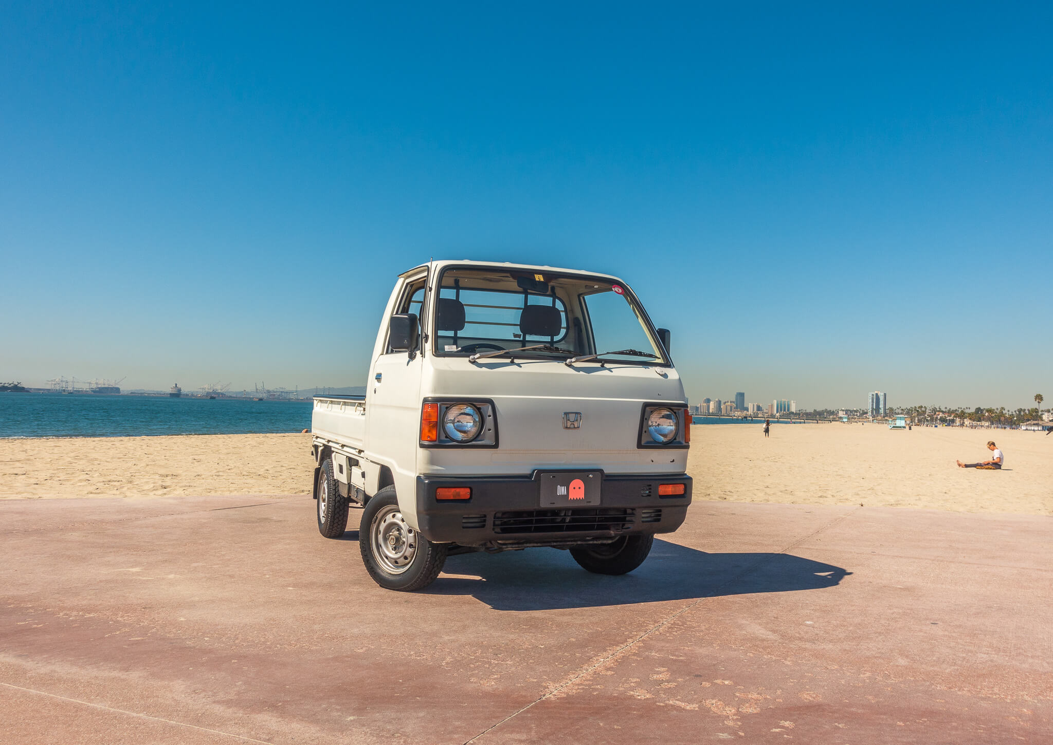 White Honda Acty Kei Truck parked on a sunny beach, showcasing its compact size, classic boxy design, and urban versatility, ideal for enthusiasts and collectors.